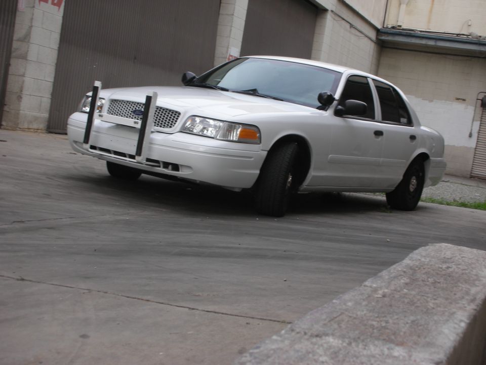 White Ford Crown Victoria with a push bumper, viewed from a low 3/4 front angle