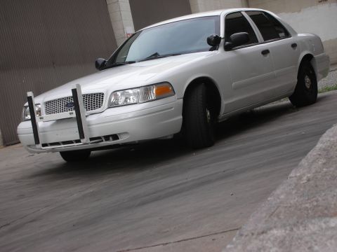 2004 Ford Crown Victoria - A white 2004 Ford Crown Victoria sedan is shown from a 3/4 front angle, equipped with a push bumper.