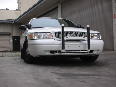 2004 Ford Crown Victoria - Front view of a white 2004 Ford Crown Victoria equipped with a push bar, parked in front of a large garage door.