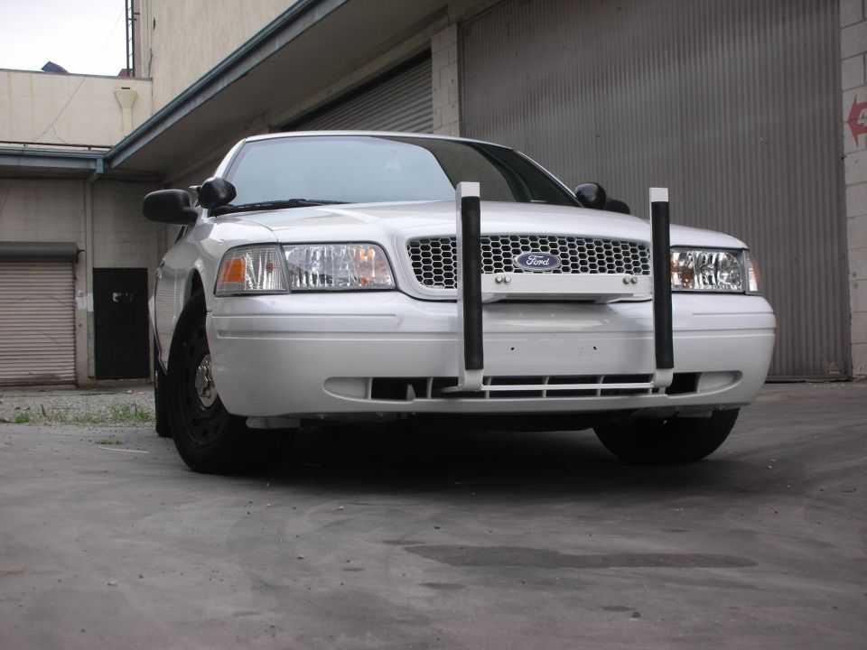 White 2004 Ford Crown Victoria with a push bar, front view, parked outside a garage