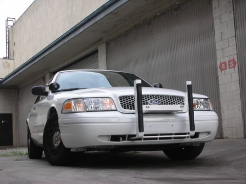 2004 Ford Crown Victoria - A white 2004 Ford Crown Victoria is parked in front of a garage door, equipped with a push bar.