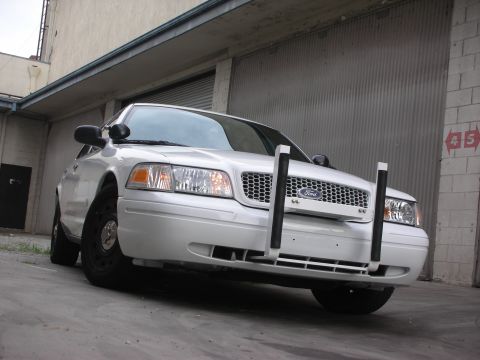 2004 Ford Crown Victoria - Front view of a white 2004 Ford Crown Victoria equipped with a push bumper, parked in front of a corrugated metal garage door.