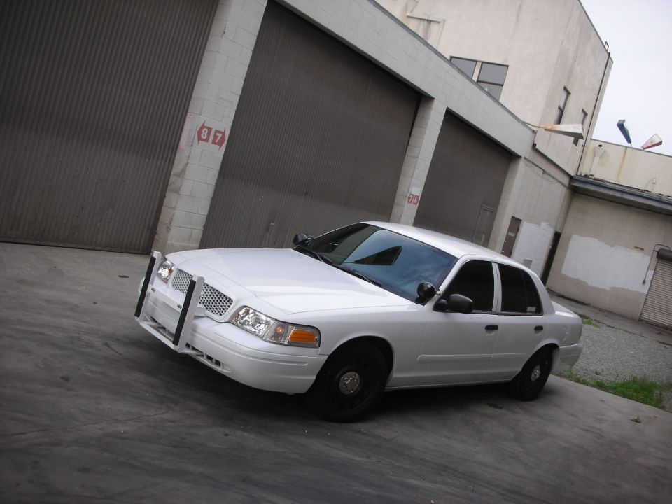 White 2004 Ford Crown Victoria with push bumper parked in front of a garage