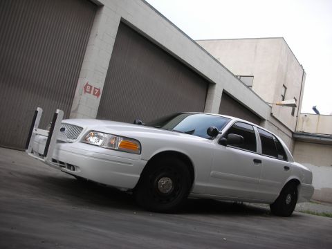 2004 Ford Crown Victoria - A white 2004 Ford Crown Victoria police car is parked in front of a large garage door.