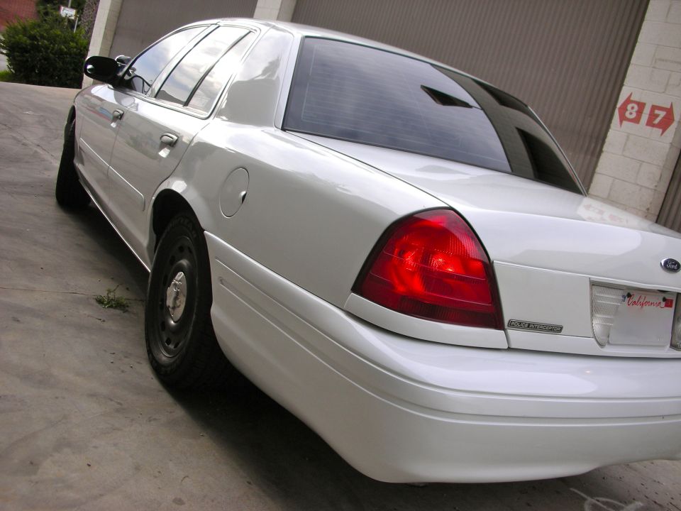 Rear quarter view of a white Ford Crown Victoria with black steel wheels and a California license plate