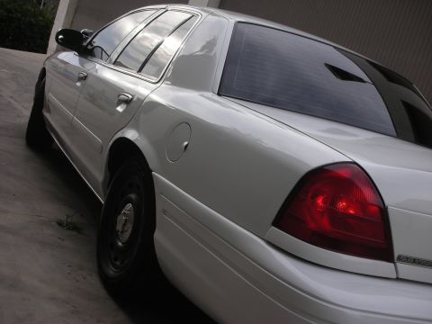 2004 Ford Crown Victoria - The rear of a white sedan is shown parked on a concrete surface, reflecting the sky.