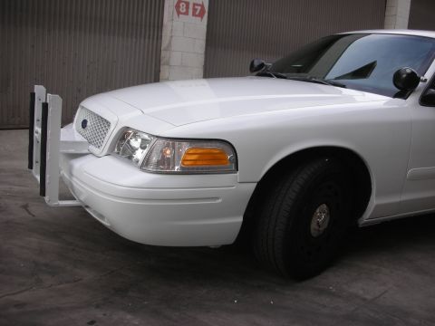 2004 Ford Crown Victoria - A white Ford Crown Victoria, likely a police vehicle, is shown from the front corner with a prominent push bumper.