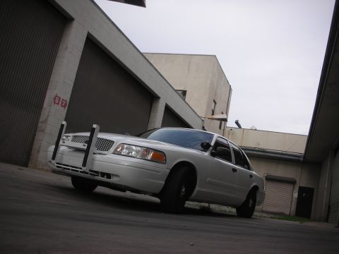 2004 Ford Crown Victoria - A white 2004 Ford Crown Victoria is parked in an alley between two buildings.