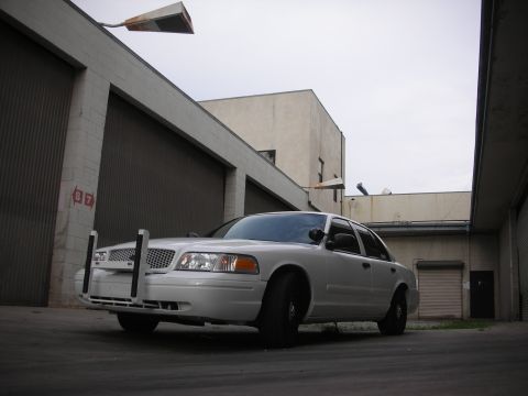 2004 Ford Crown Victoria - A white 2004 Ford Crown Victoria police car is parked in front of a garage with a push bumper attached.