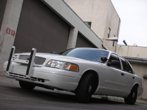2004 Ford Crown Victoria - A white Ford Crown Victoria, likely a police interceptor, is parked in front of a large garage door.