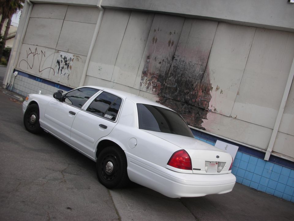 White 2004 Ford Crown Victoria parked next to a graffiti-covered wall