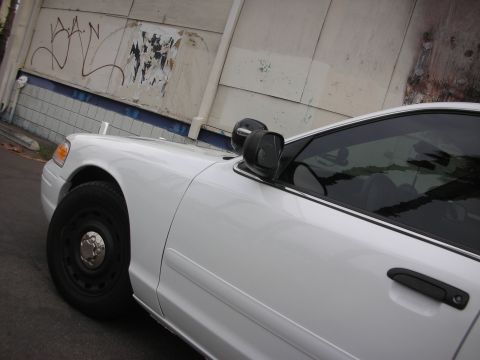 2004 Ford Crown Victoria - A white 2004 Ford Crown Victoria is parked in front of a graffiti-covered wall.