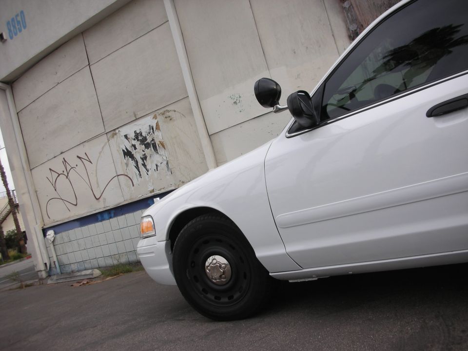 White sedan side view, parked near a graffiti-covered wall