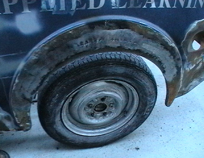 Rear wheel arch and tire of a dark vehicle with visible bodywork modifications