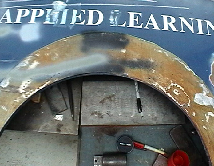 Wheel well interior showing rust damage and metal patch repairs. Marker and measuring tool visible