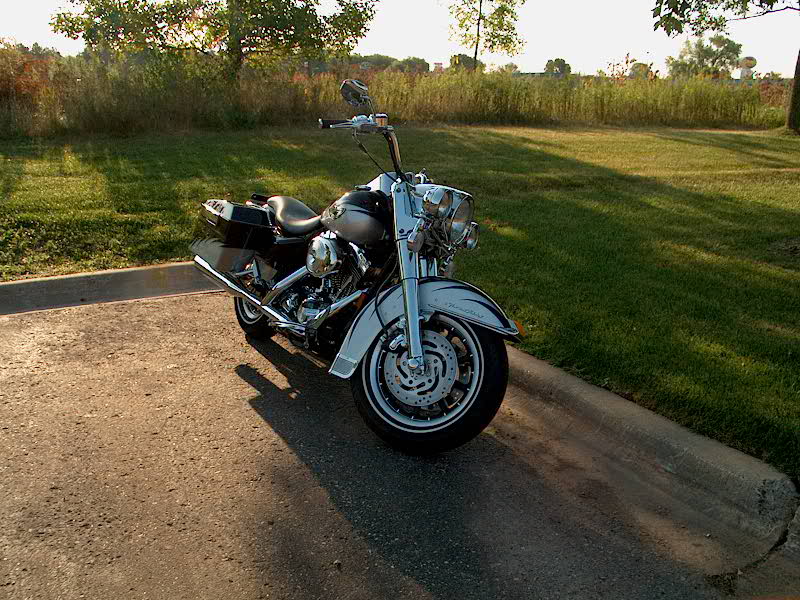 Black and silver Harley touring motorcycle parked by a field at sunset