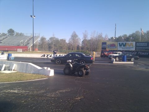 2001 Ford Crown Victoria - A black 2001 Ford Crown Victoria and an ATV are lined up on a drag strip under a clear blue sky.