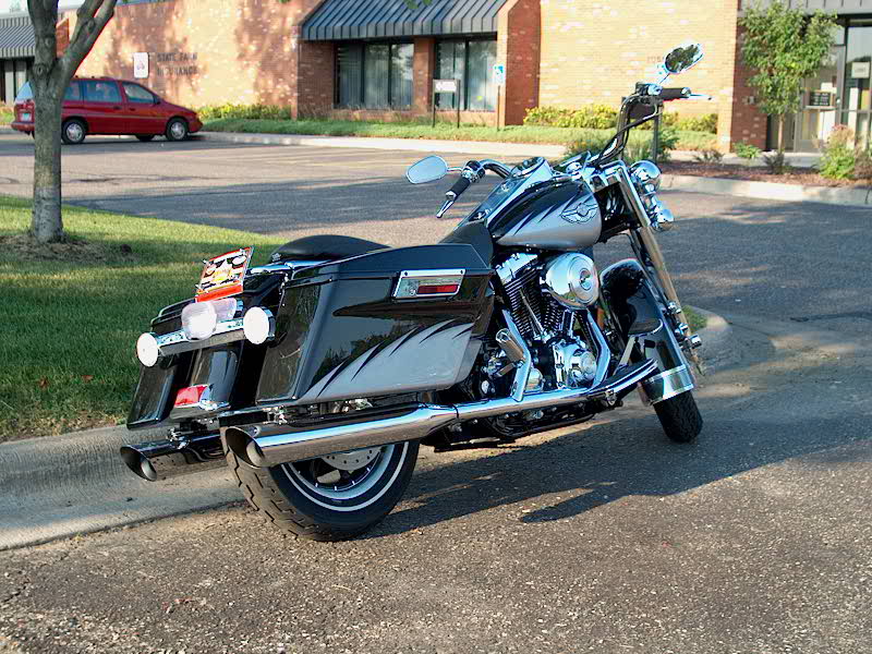Black Harley-Davidson bagger motorcycle from rear three-quarter at curb with chrome pipes and saddlebags
