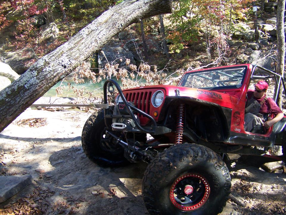 Red Jeep modified for off-roading, parked on a dirt trail with a fallen tree across the scene