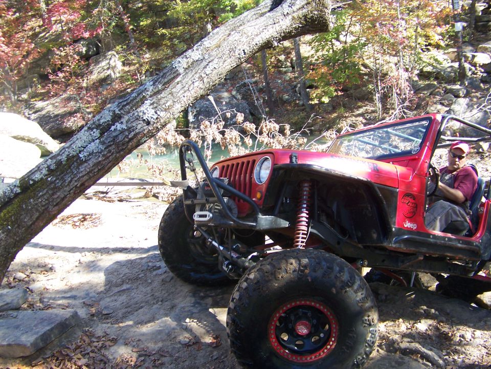 Red off-road Jeep with large tires and roll cage, parked on rocky terrain
