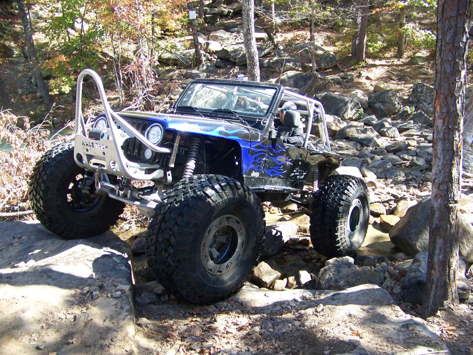 Blue and black off-road Jeep with custom bumper and large tires navigating rocky terrain