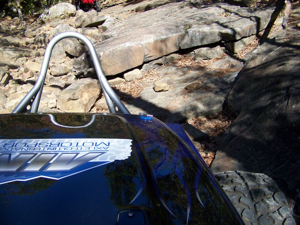 Buggy with roll cage and 'AXLETECHNOLOGY MOTORSPORTS' decal navigating a rocky trail