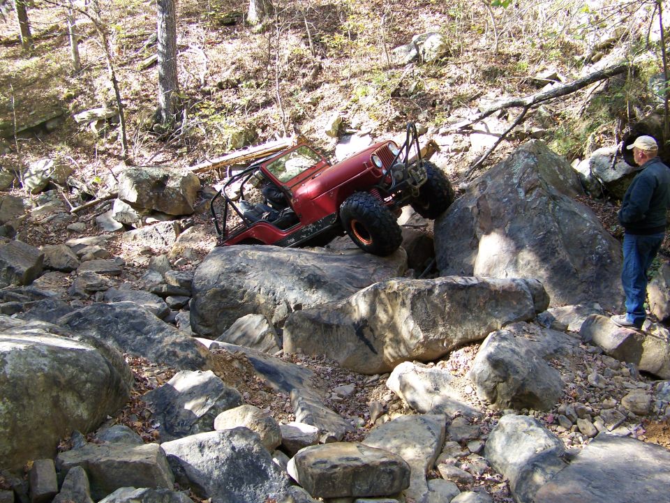 Red off-road vehicle with roll cage on large rocks, driver visible