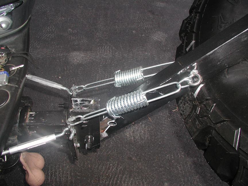 Two zinc coil springs on threaded rods mounted to black bracket near off-road tire