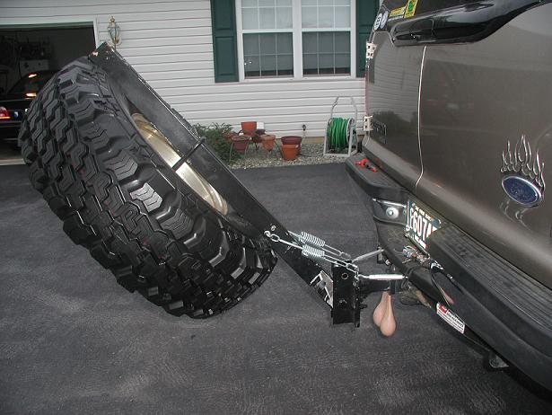Rear hitch-mounted swing-out spare tire carrier with mud tire on tan SUV