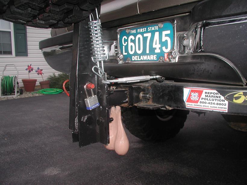 Rear hitch of dark SUV with Delaware plate, padlock, and novelty accessory in driveway