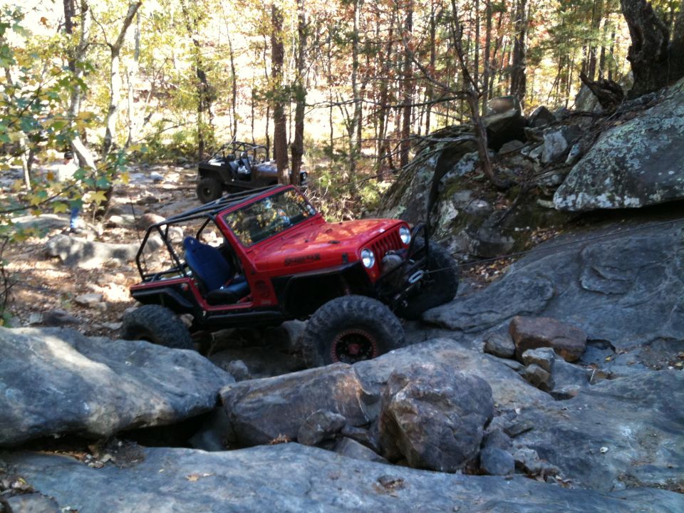 Red Jeep Wrangler navigating rocky terrain with another off-road vehicle in the background