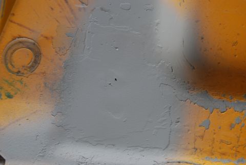 1982 Ford Bronco - This image shows a section of painted metal with areas of primer and peeling paint, along with a circular marking.