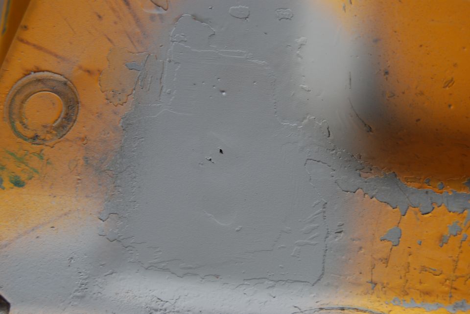 Close-up of a painted metal surface with peeling paint and a circular indentation