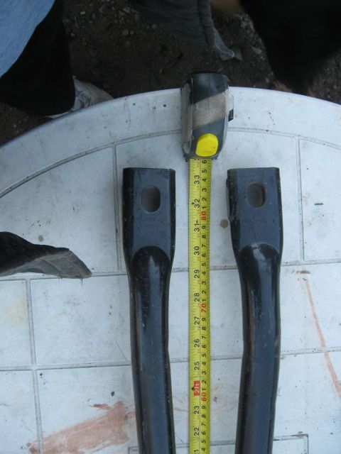 1981 Ford Bronco - Two black metal parts are measured with a tape measure, with a watermark for SuperMotors.net visible.