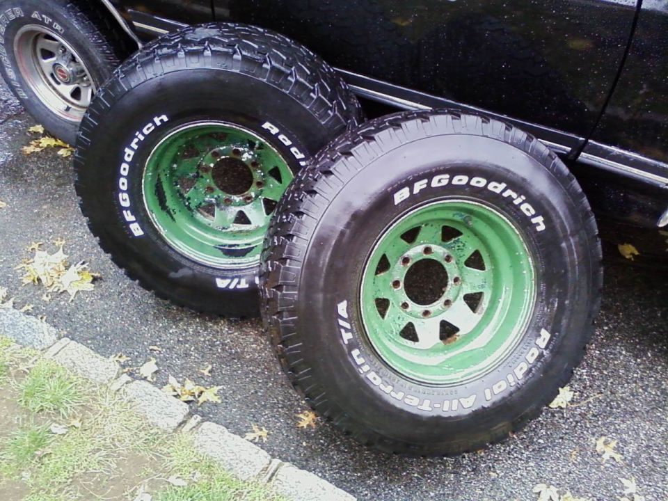Two BFGoodrich All-Terrain T/A tires mounted on green 5-lug rims, with a black vehicle in the background