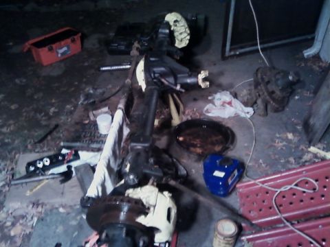 1990 Ford Bronco - A disassembled vehicle axle assembly is shown on the ground, surrounded by tools and automotive fluids.