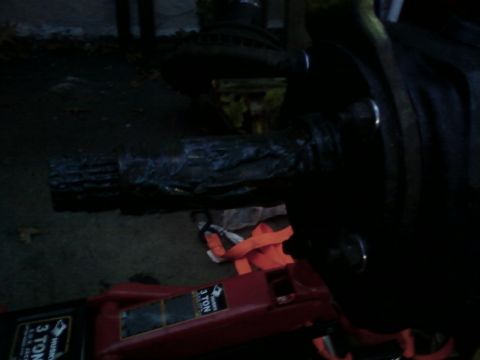 1990 Ford Bronco - Dim outdoor shot of a heavy axle housing tube and its cast center section resting on pavement, supported by a red Husky 3-ton floor jack wi…