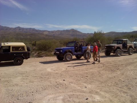 1996 Ford Bronco - A group of Ford Broncos are parked on a dirt road in a desert landscape under a clear blue sky.