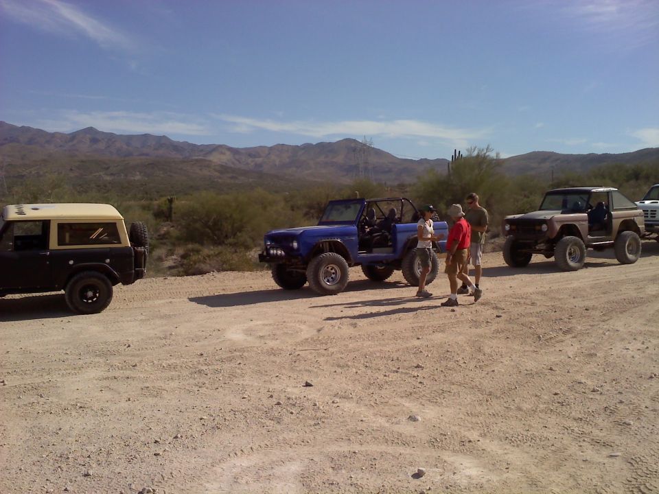 Several Ford Broncos parked on a dirt road in a desert with mountains in the background