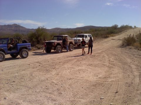 1996 Ford Bronco - Several vehicles are parked on a dusty desert road under a clear blue sky.