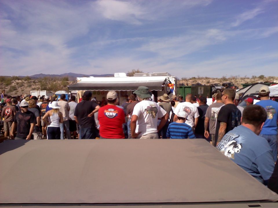 Outdoor gathering with many people, tents, and a food truck under a partly cloudy sky