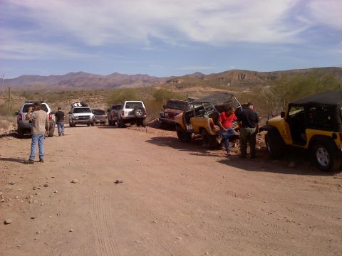 1996 Ford Bronco - A group of off-road vehicles are gathered on a dirt road with mountains in the background.