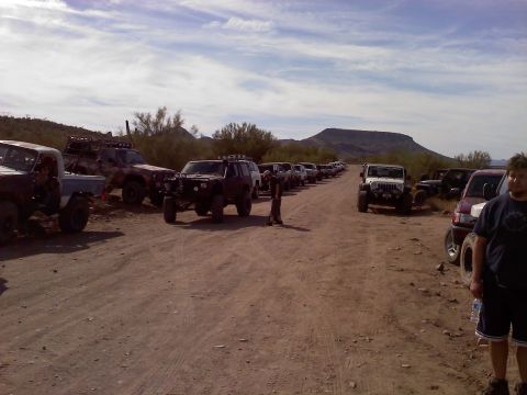 1996 Ford Bronco - A group of off-road vehicles are parked on a dirt road with mountains in the background under a cloudy sky.