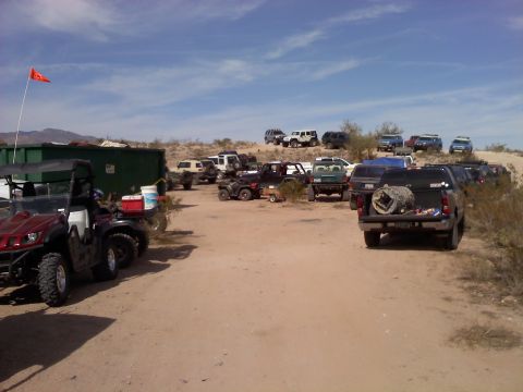 1996 Ford Bronco - A variety of off-road vehicles are parked in a dusty lot under a bright, partly cloudy sky.