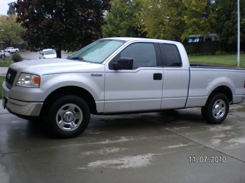 1996 Ford Bronco - A silver pickup truck is parked on a wet driveway with trees in the background.