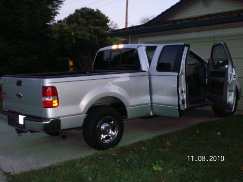 1996 Ford Bronco - A silver four-door pickup truck is parked in a driveway with its passenger doors open.