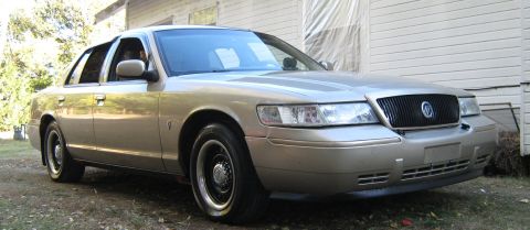 2000 Mercury Grand Marquis - A gold Mercury Grand Marquis is parked in front of a house with siding.