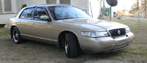 2000 Mercury Grand Marquis - A gold 2000 Mercury Grand Marquis is parked on a gravel driveway in front of a house.