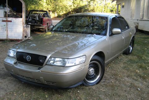 2000 Mercury Grand Marquis - A gold 2000 Mercury Grand Marquis is shown from the front three-quarter view, parked outdoors on a grassy area.