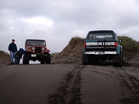 1996 Ford Bronco - Two off-road vehicles parked on sand dunes under a cloudy sky.